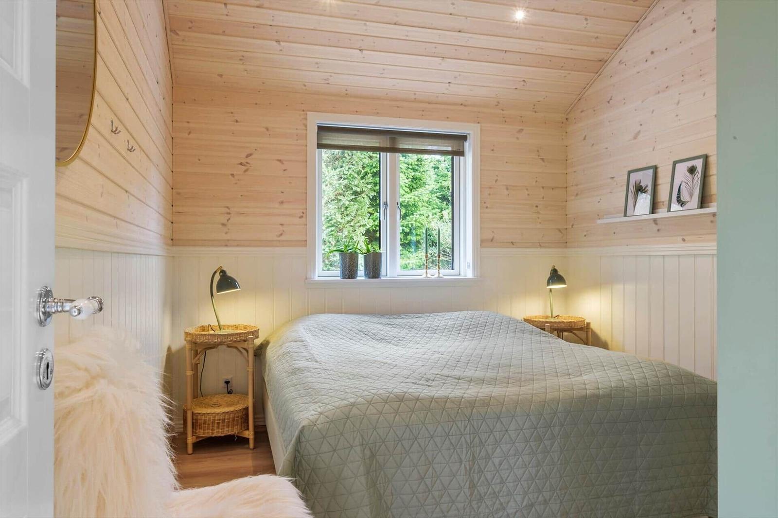 Bedroom with wooden walls, window, and bed with coverlet.