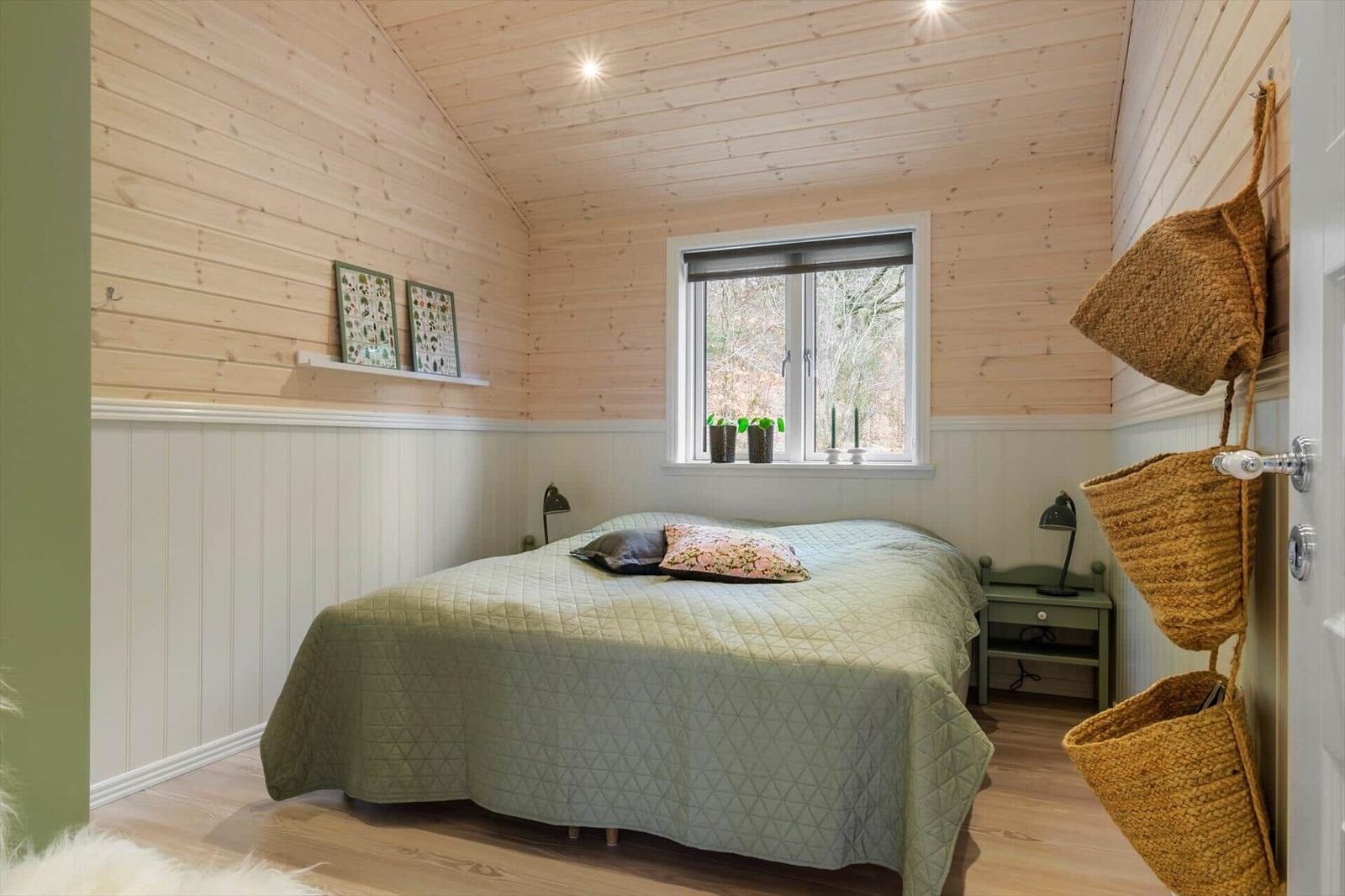 Bedroom with wooden walls, bed, and window with view of forest.