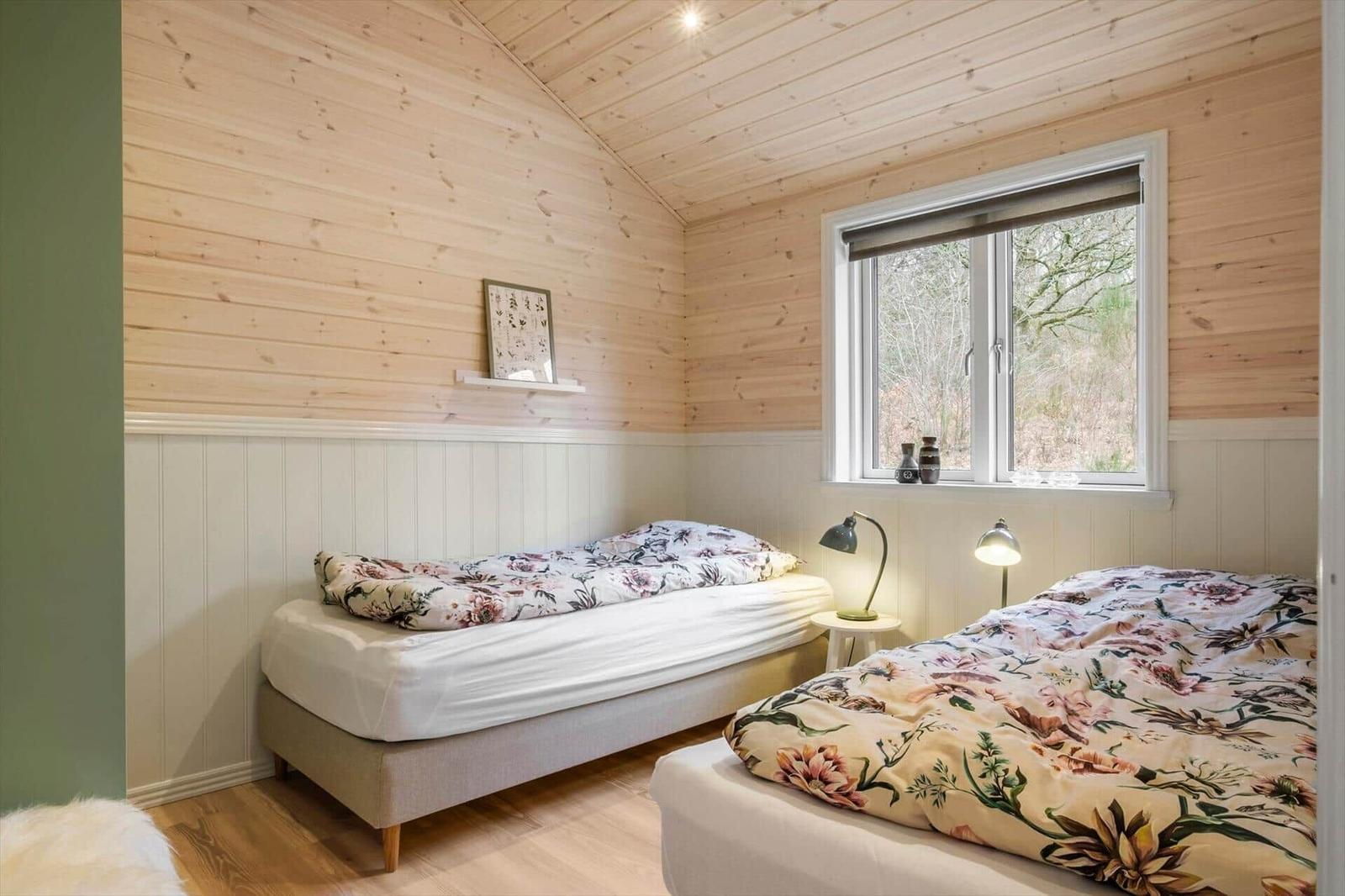 Two beds with floral bedding, wooden walls, and window with view of forest.