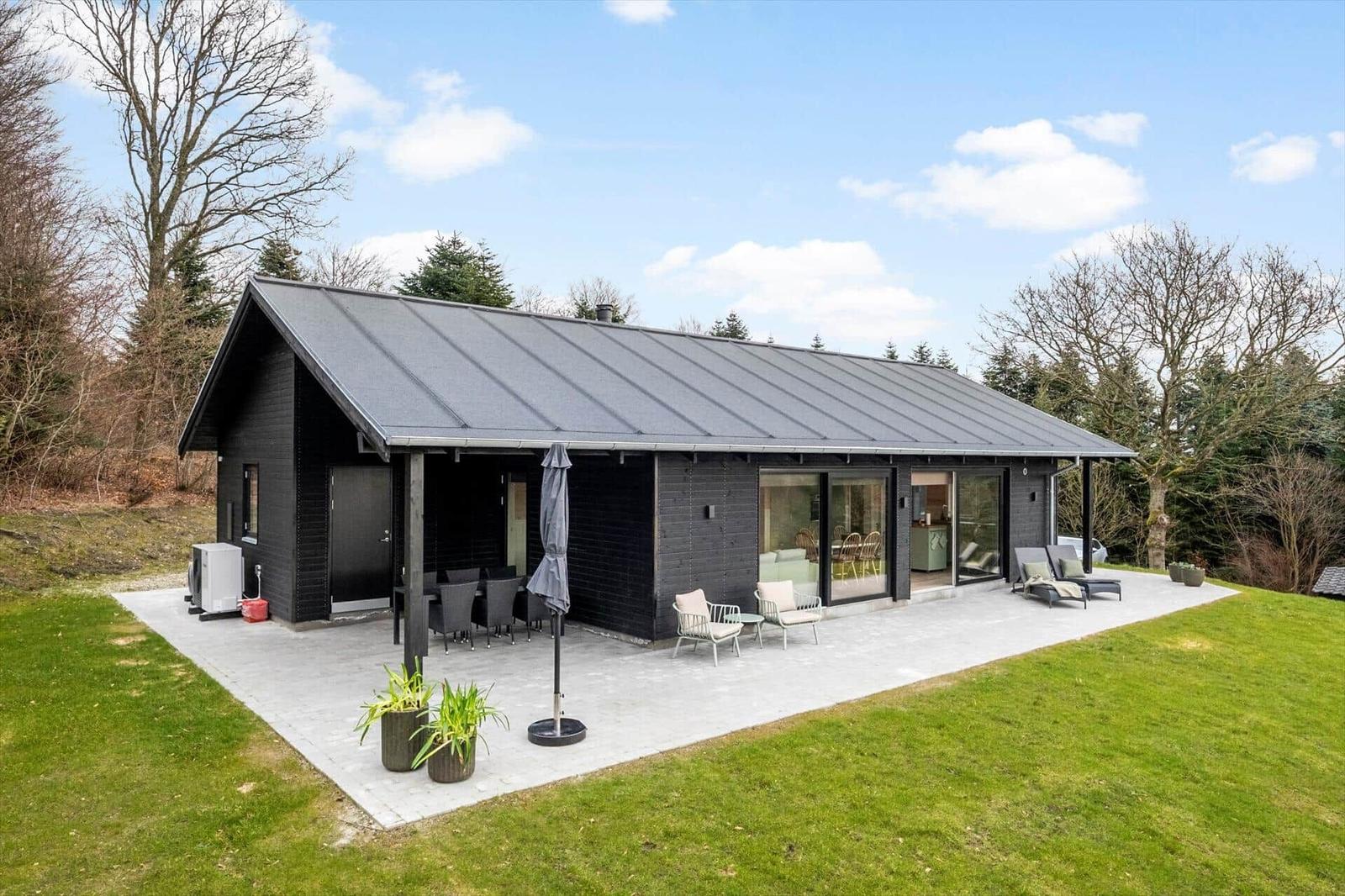 Modern villa with terrace, garden, and glass facade. Outdoor seating and plants.