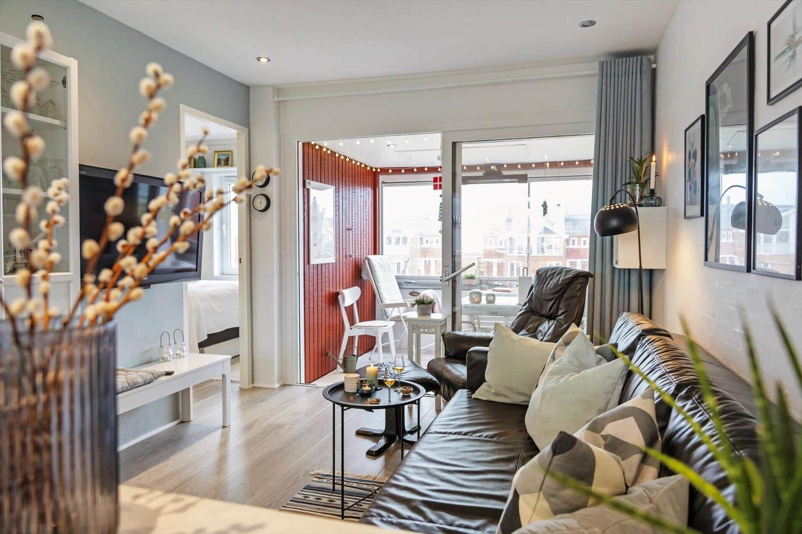 Wohnzimmer mit Ledersofa, Fernseher und Blick auf Balkon mit Stühlen.
