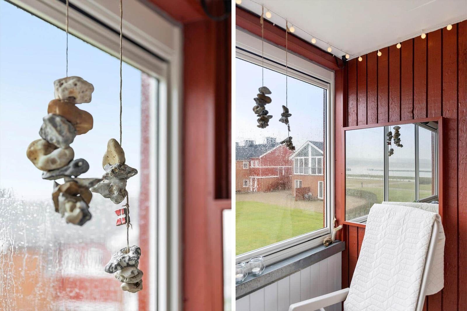 Fenster mit Steinanhänger und Sicht auf Haus und Grünfläche.
