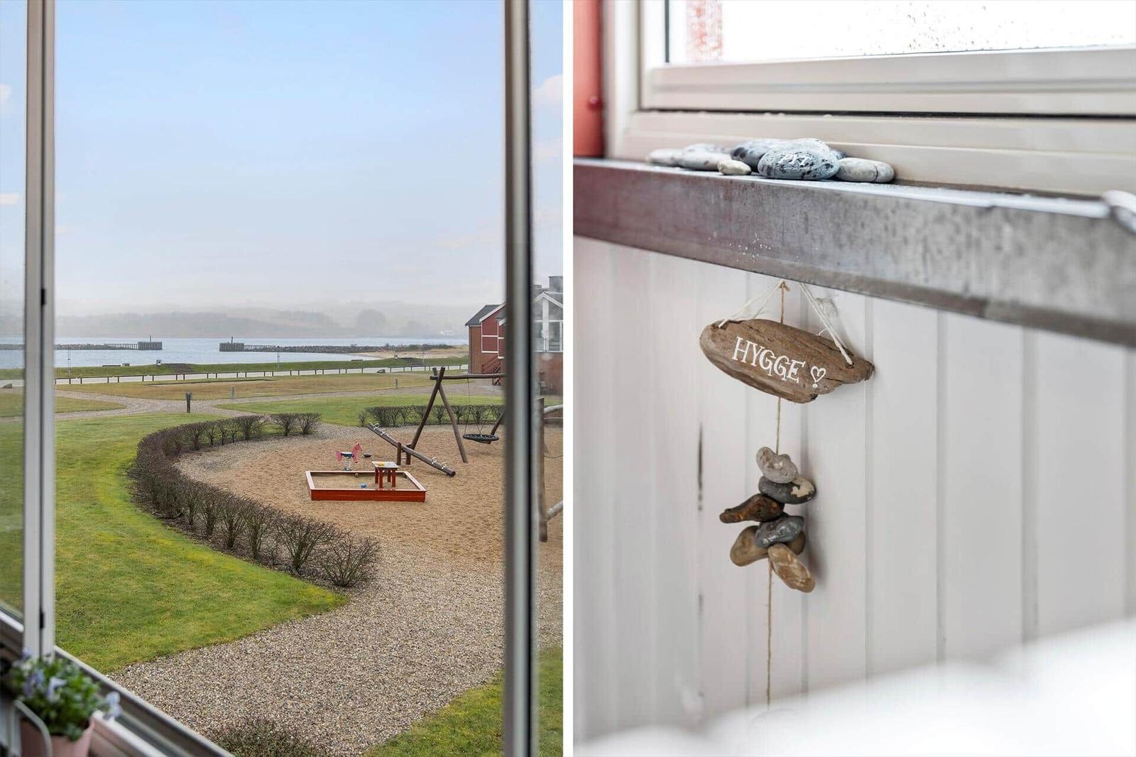Blick auf Spielplatz und Wasser, Hängeschild mit Steinen an Fenster.