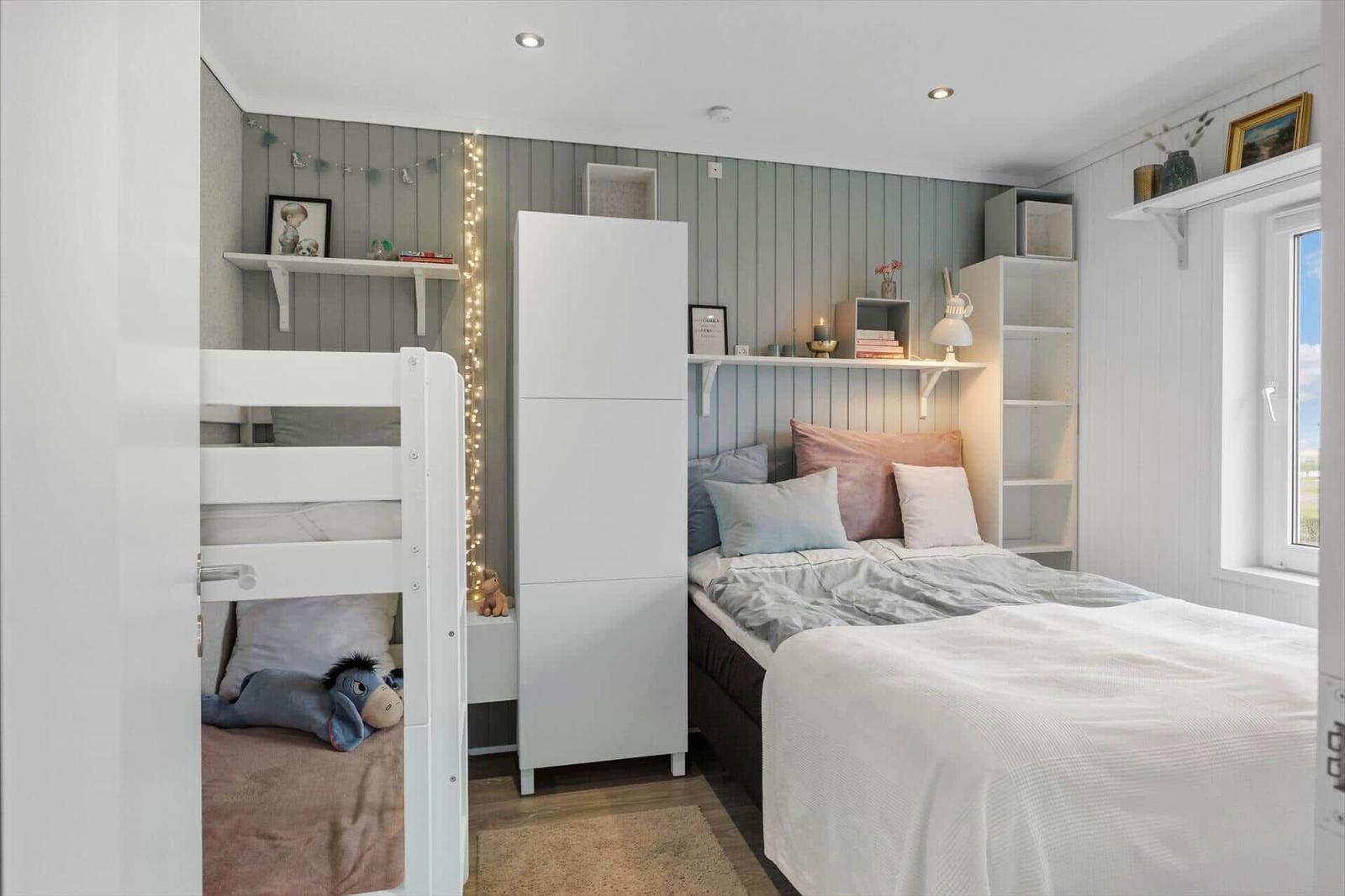 Schlafzimmer mit Doppelbett, Hochbett und weißen Regalen an der Wand.