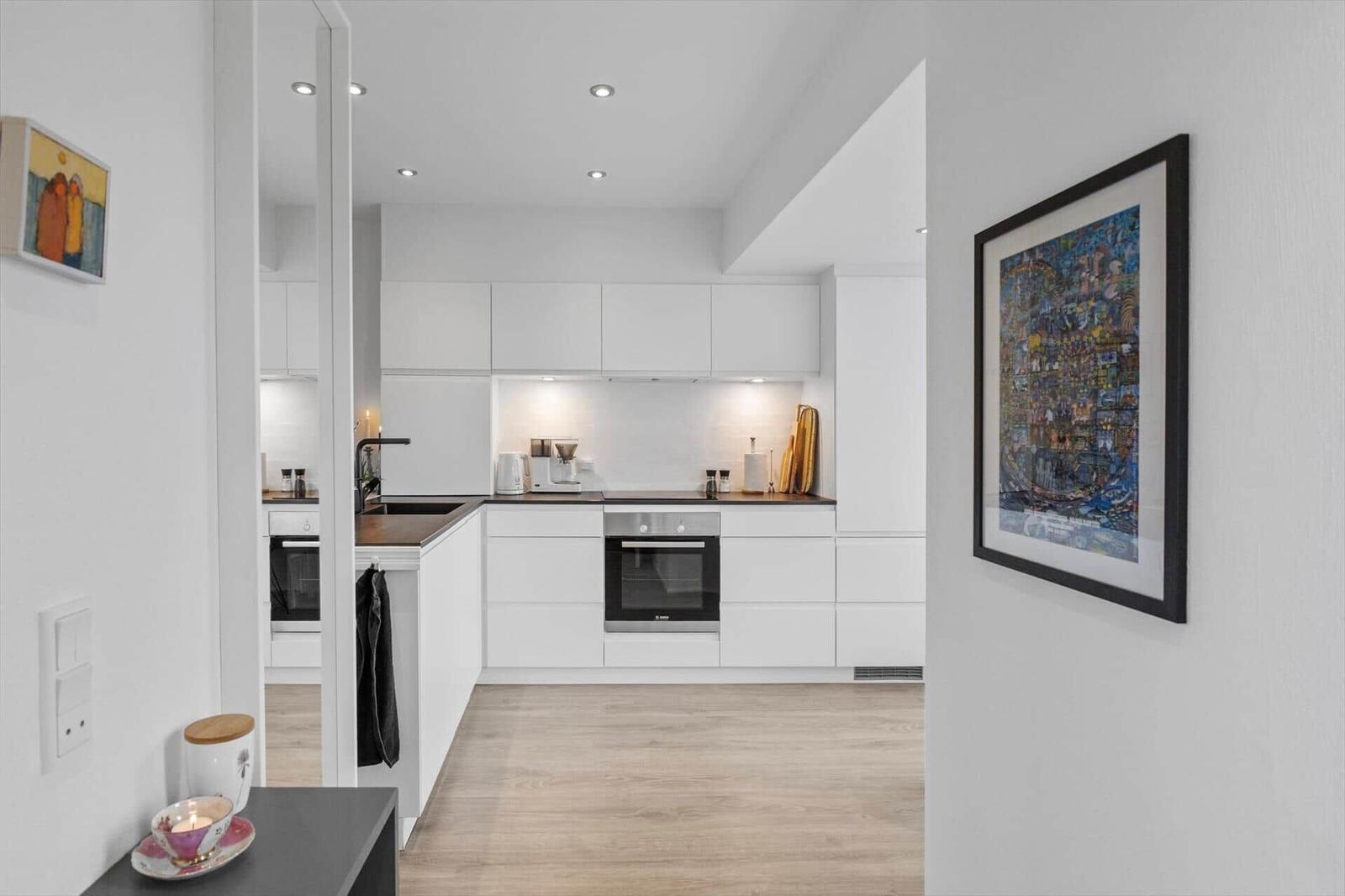Moderne Küche mit weißen Schränken und Holzboden. Aufgehängte Bilder schmücken die Wände.