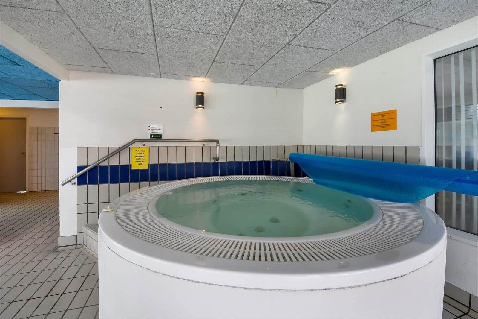 Innenpool mit Whirlpool und blauer Plane, Wand mit Schildern und Handlauf.