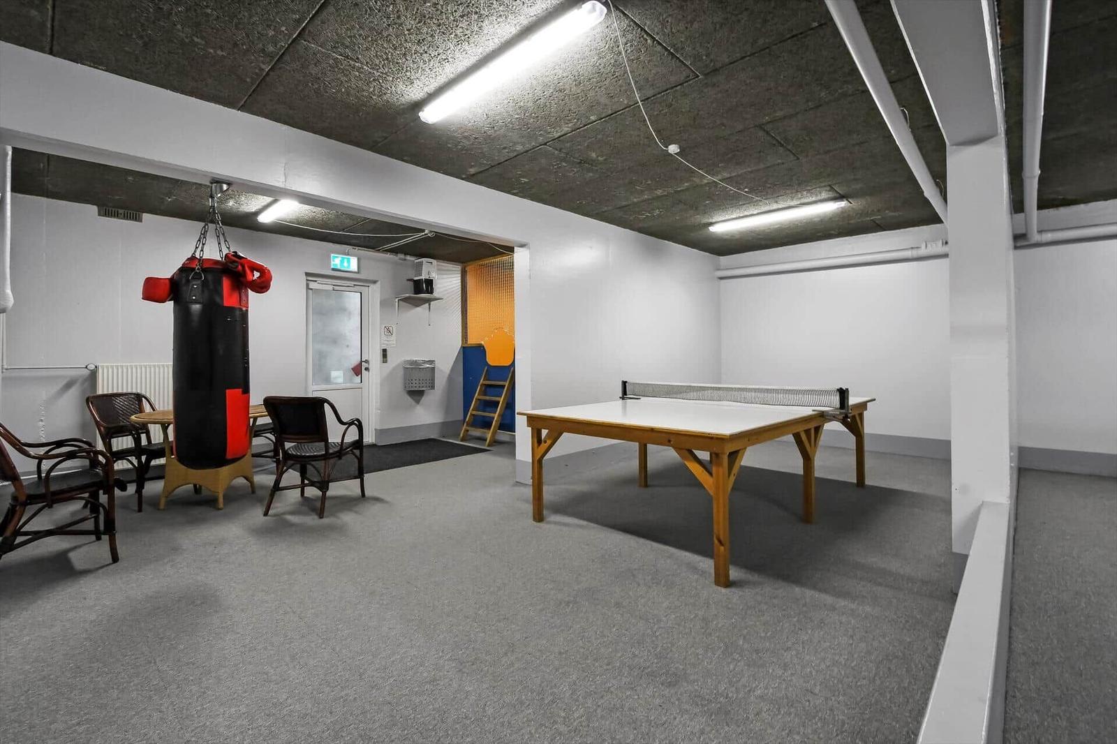 Raum mit Tischtennisplatte und Boxsack. Weiße Wände, grauer Boden und Deckenleuchten.