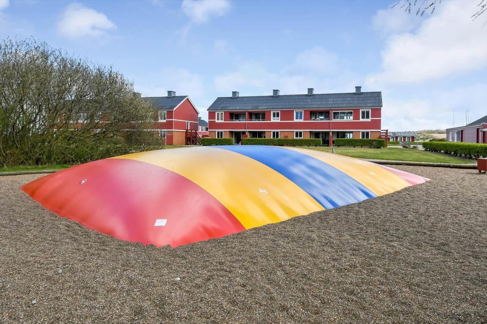 Farbiger Spielplatz vor rotem Ferienhaus mit Grünflächen.