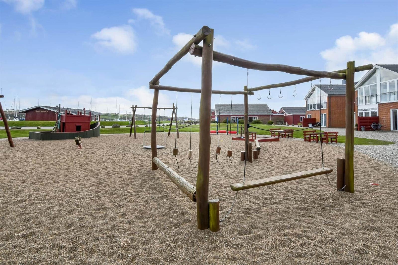 Großer Sandplatz mit Holzspielgeräten und Rutschbahn im Hintergrund.