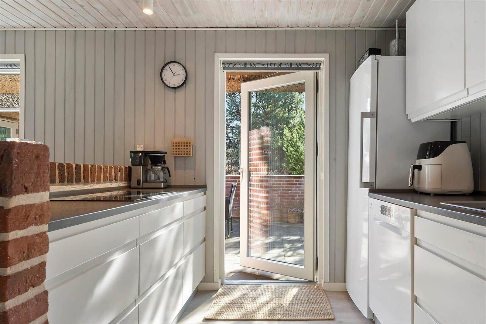 Küche mit weißer Einbauküche, Kühlschrank und Tür zum Garten.