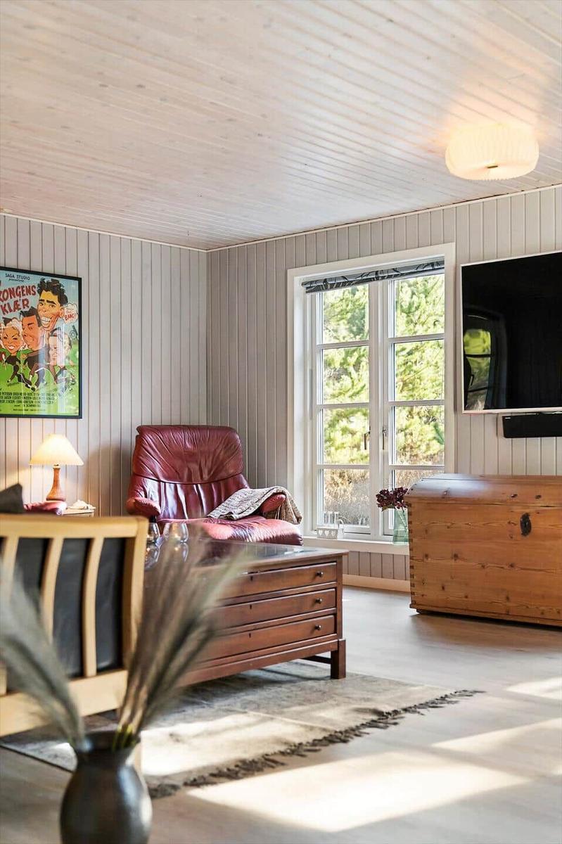 Ein Wohnzimmer mit rotem Ledersessel, Holzmöbeln und Fenster zur grünen Außenseite.