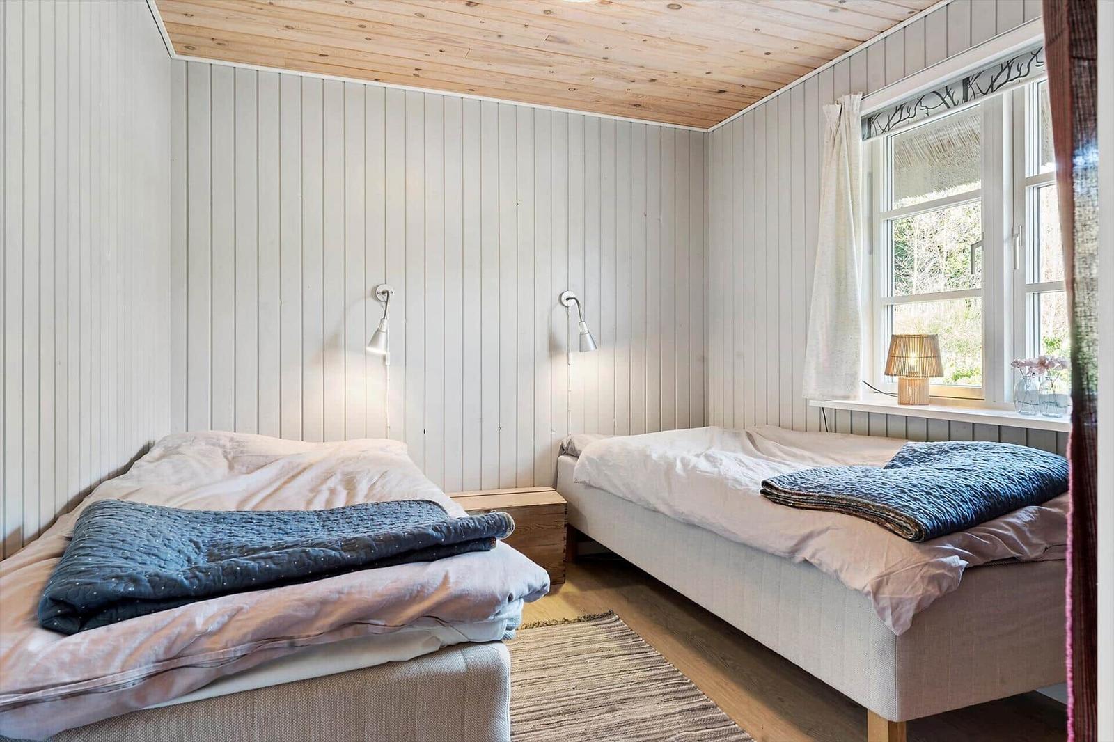 Zwei Betten mit Bettwäsche und Decken. Holzwand und Fenster mit Vorhang.