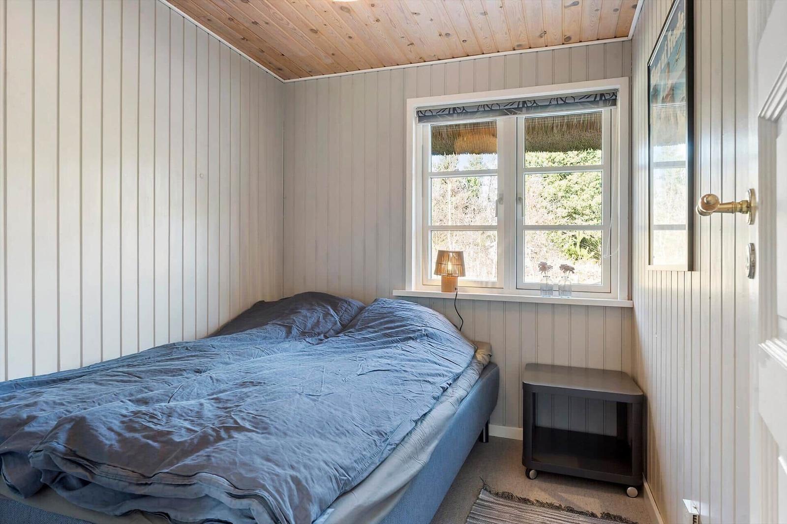 Schlafzimmer mit Bett, Fenster und Nachttisch.