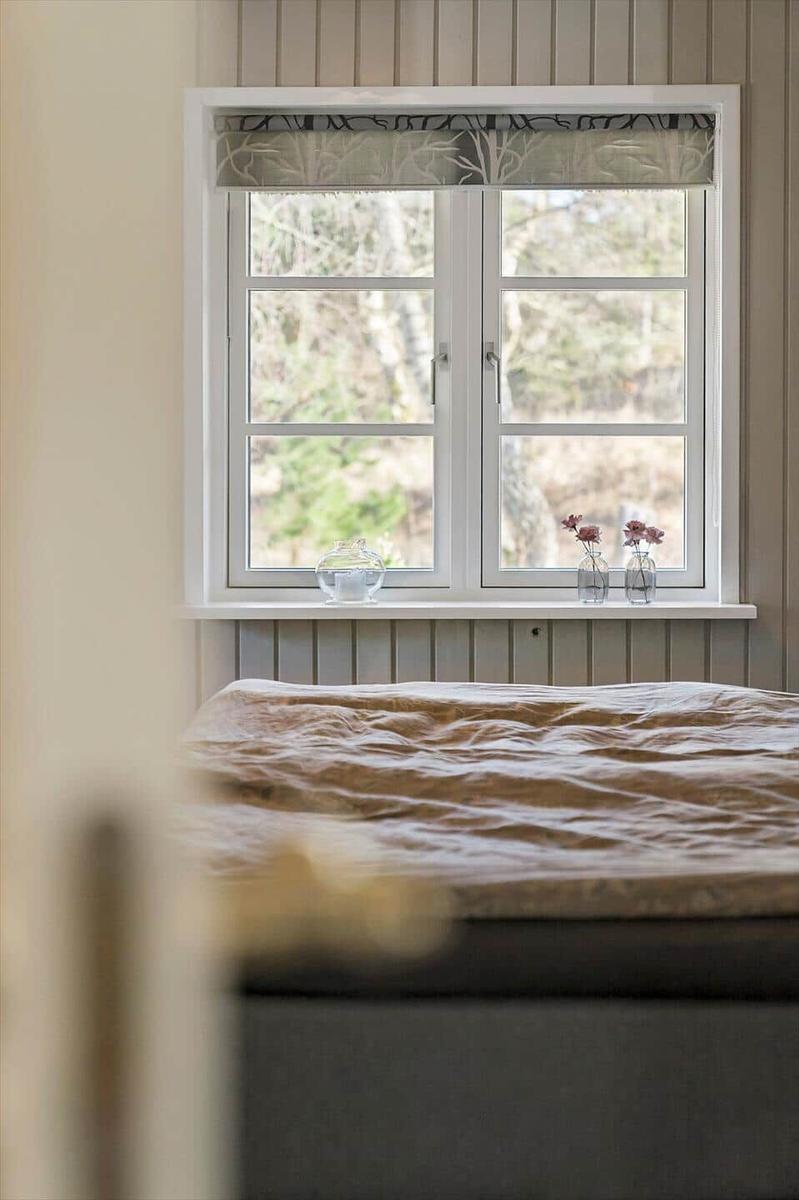 Ein Bett vor einem Fenster mit Waldblick und Blumenvasen.