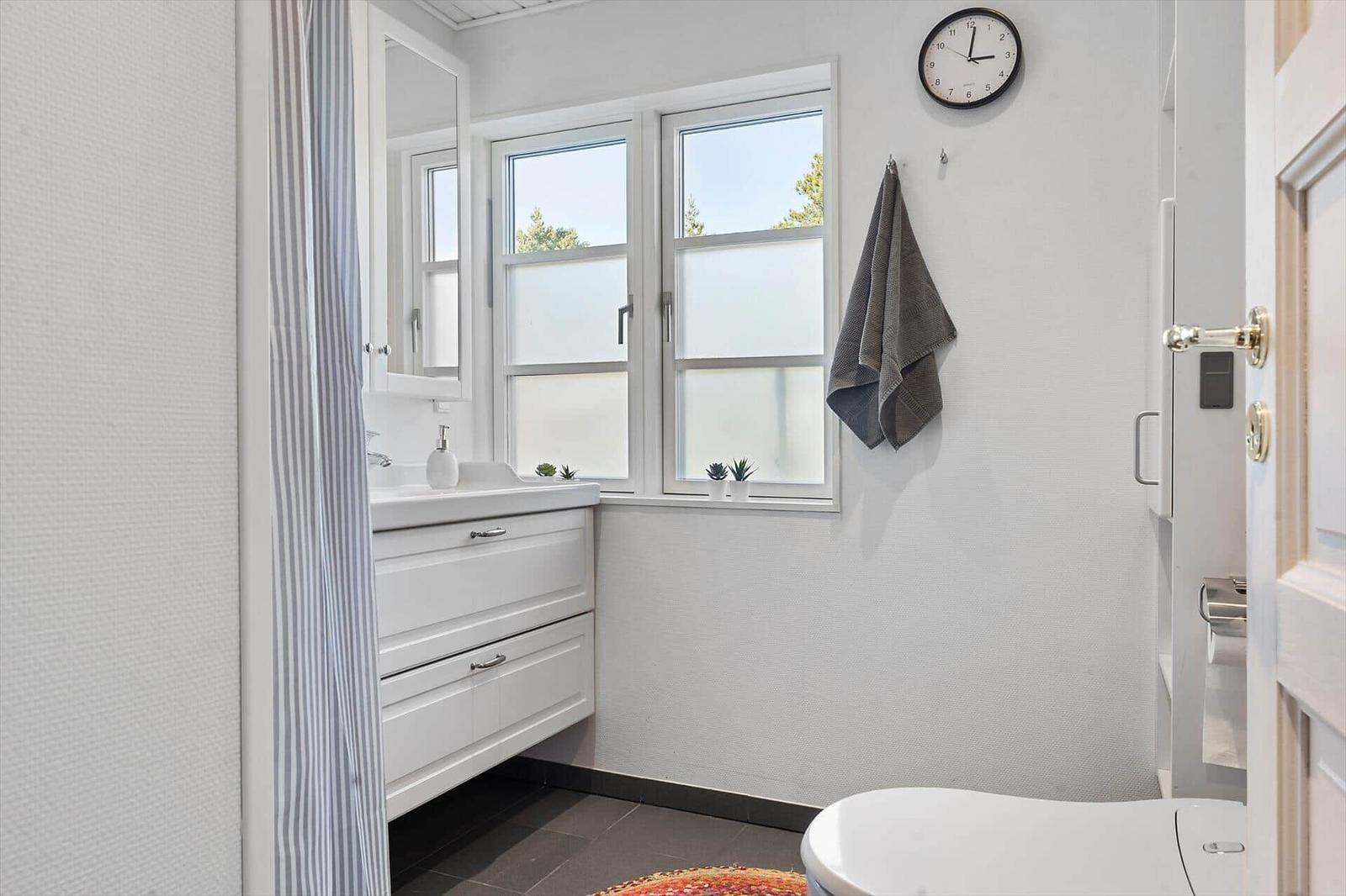 Badezimmer mit Waschbecken, Fenster, Uhr und Toilette.