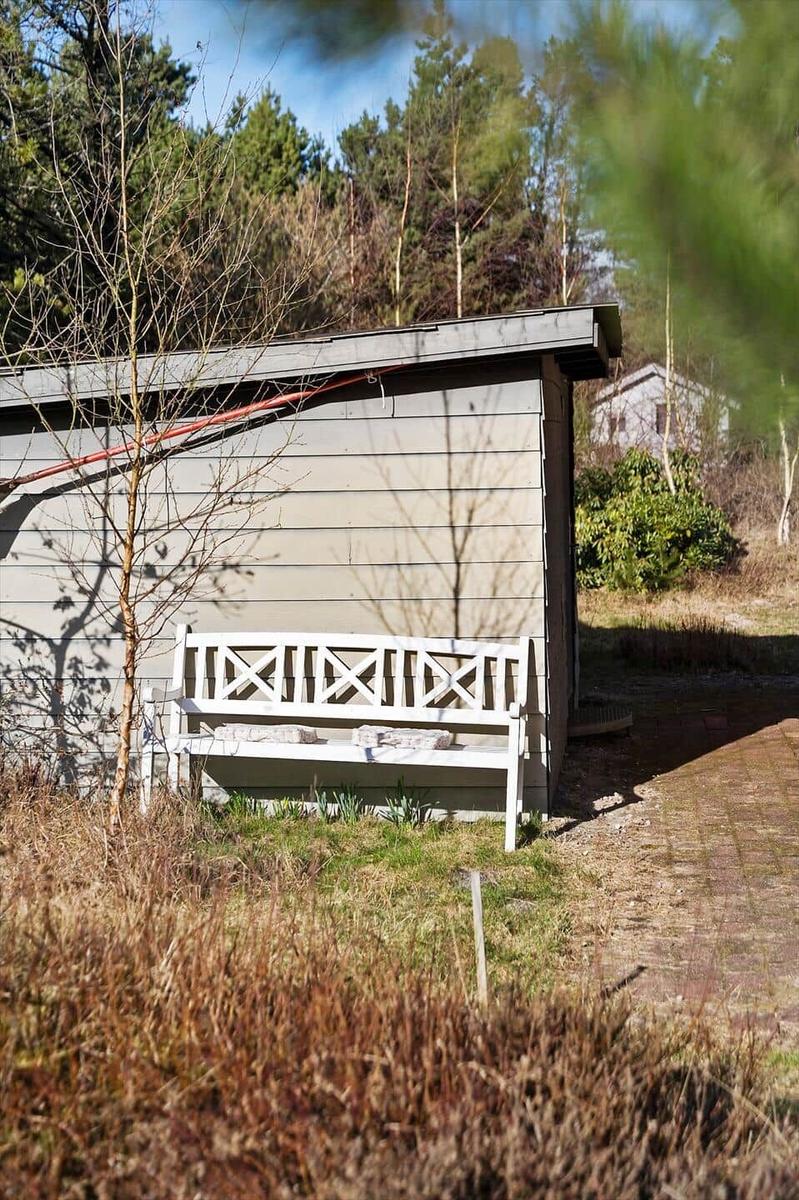 Weißer Holzstuhl vor einem grauen Holzhaus in einer grünen Umgebung.