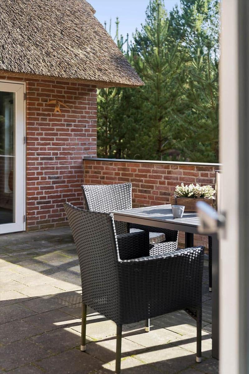 Terrasse mit Tisch und Stühlen vor einem Haus mit Strohdach und Backsteinmauer.