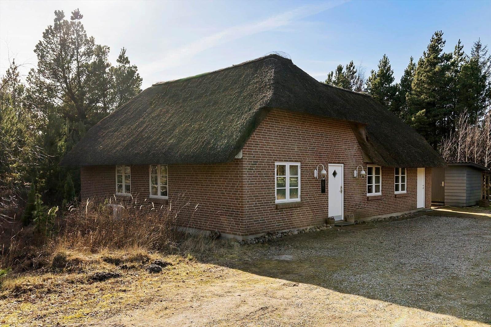 Ein Haus mit Strohdach und Backsteinfassade, umgeben von Bäumen und einem Kiesweg.