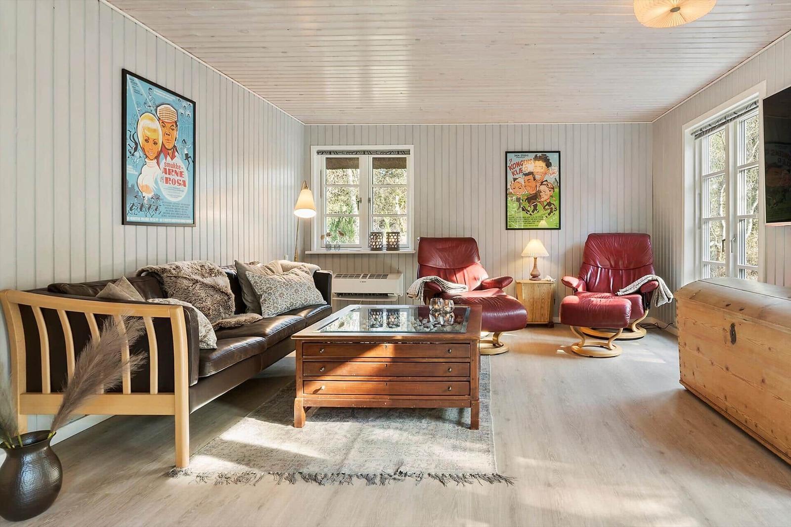 Wohnzimmer mit Sofa, zwei roten Sesseln, Couchtisch und Wandbildern.