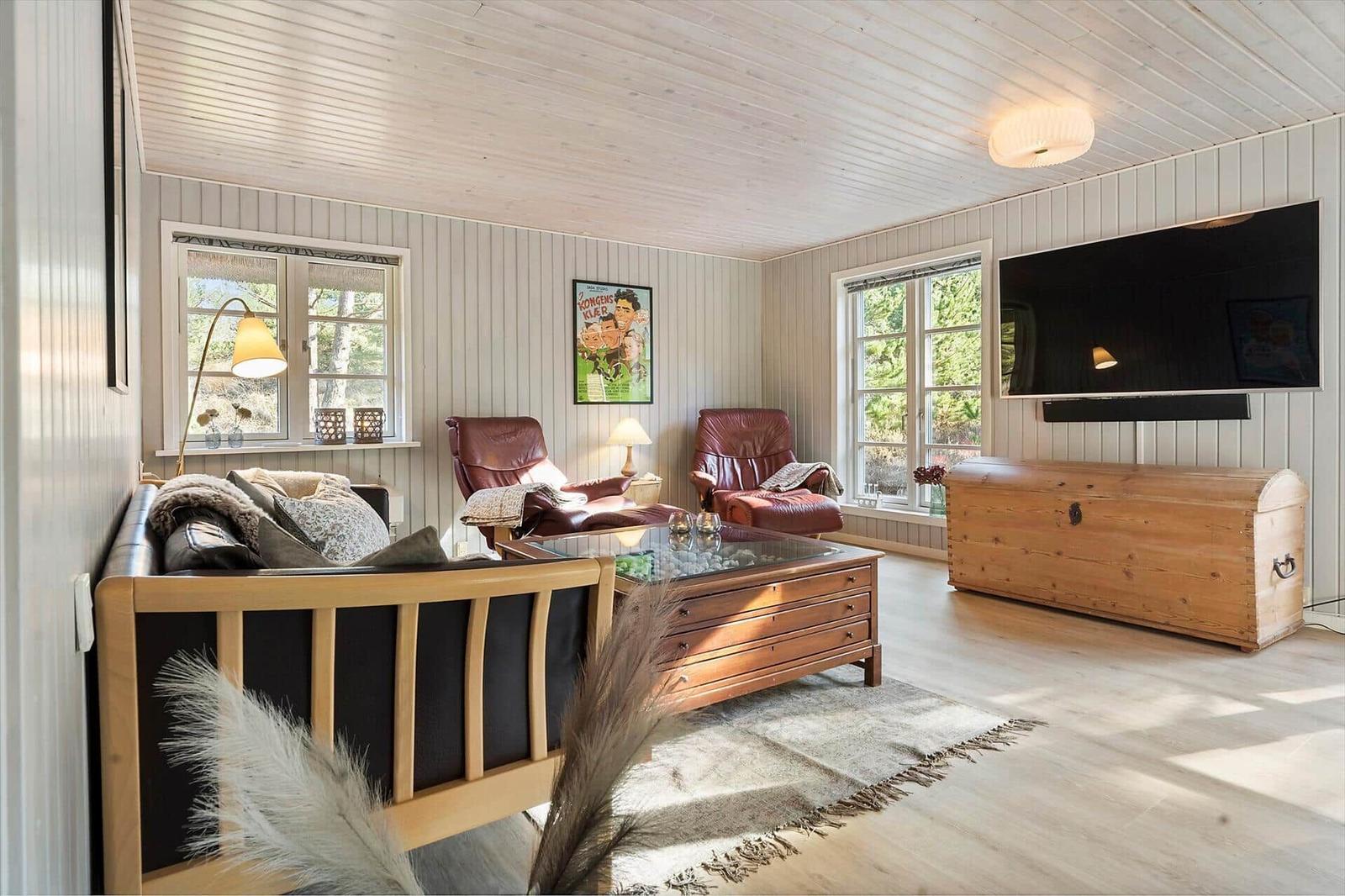 Wohnzimmer mit Sofa, zwei Ledersessel, Fernseher und Holztruhe.