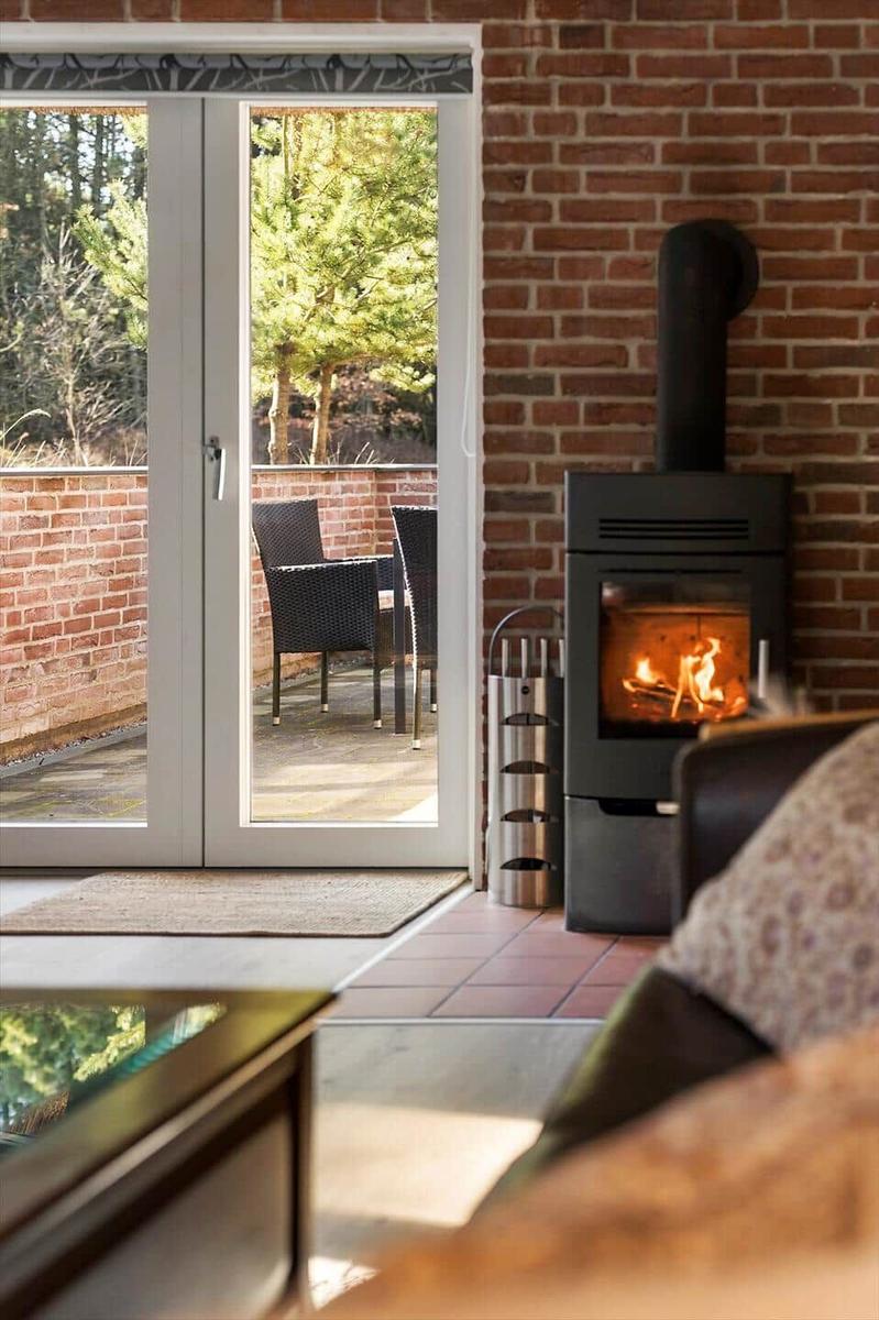 Ein Kamin mit brennendem Holz neben einer Glastür zum Garten.