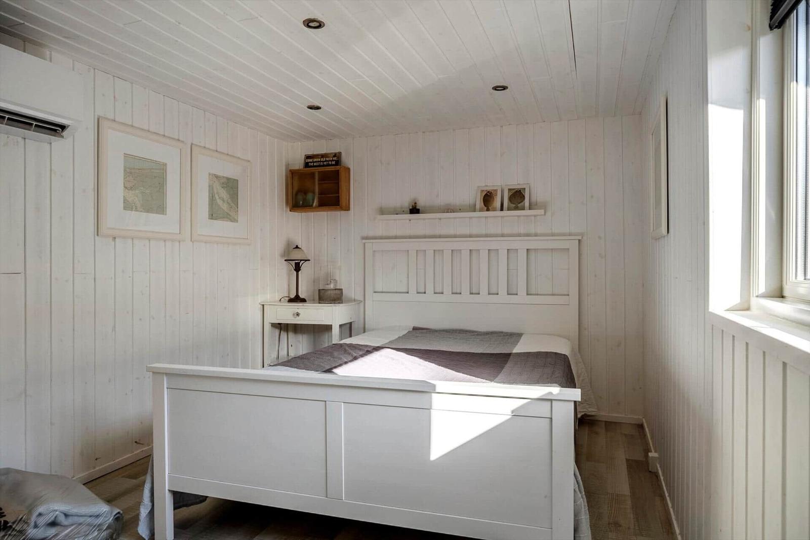 Bedroom with white bed, wood walls, and window