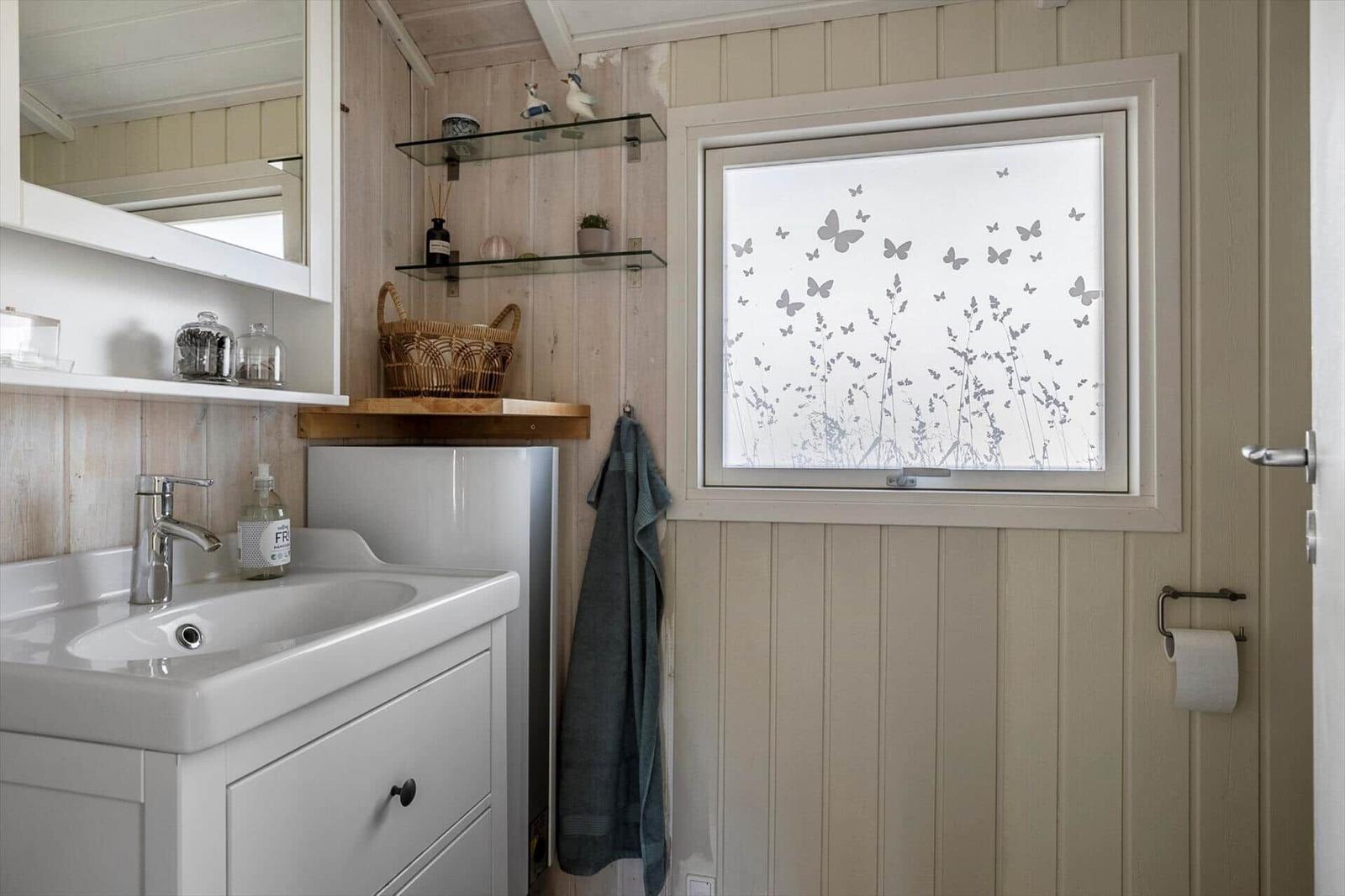 Bathroom with sink, mirror, and window with butterfly motif.