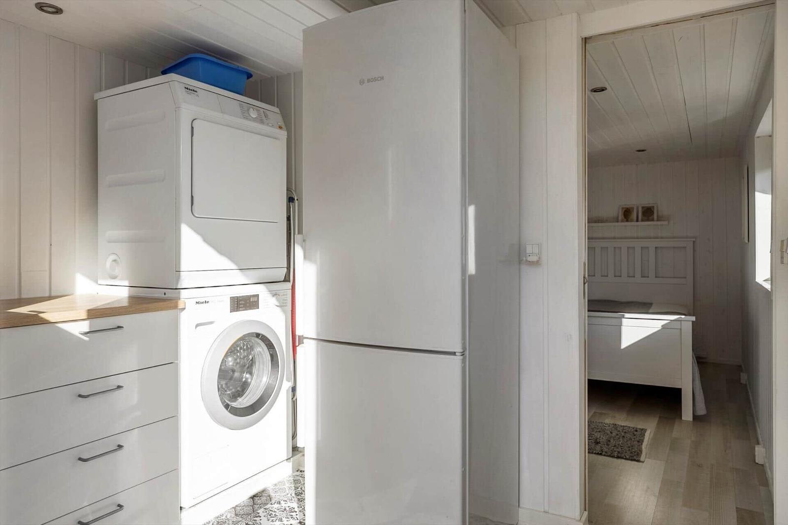 Kitchen with washing machine, dryer, and refrigerator. Corridor leading to bedroom with bed.