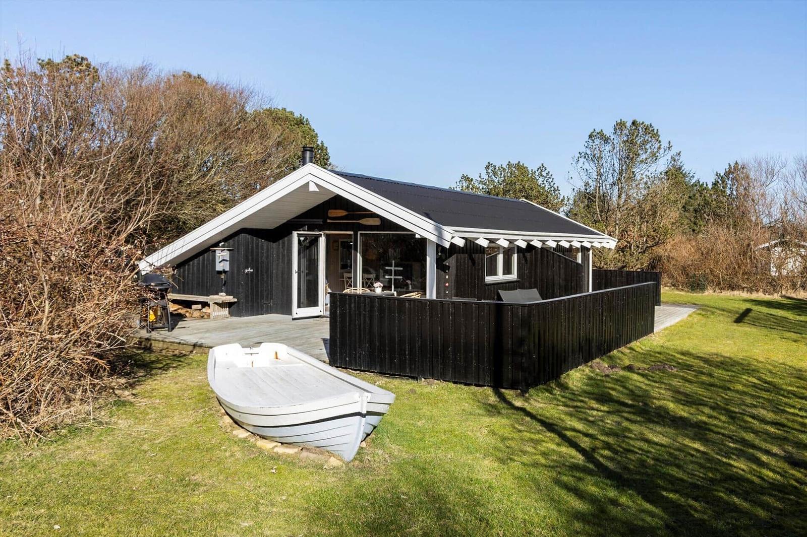 Black wooden house with terrace and white boat on grass.