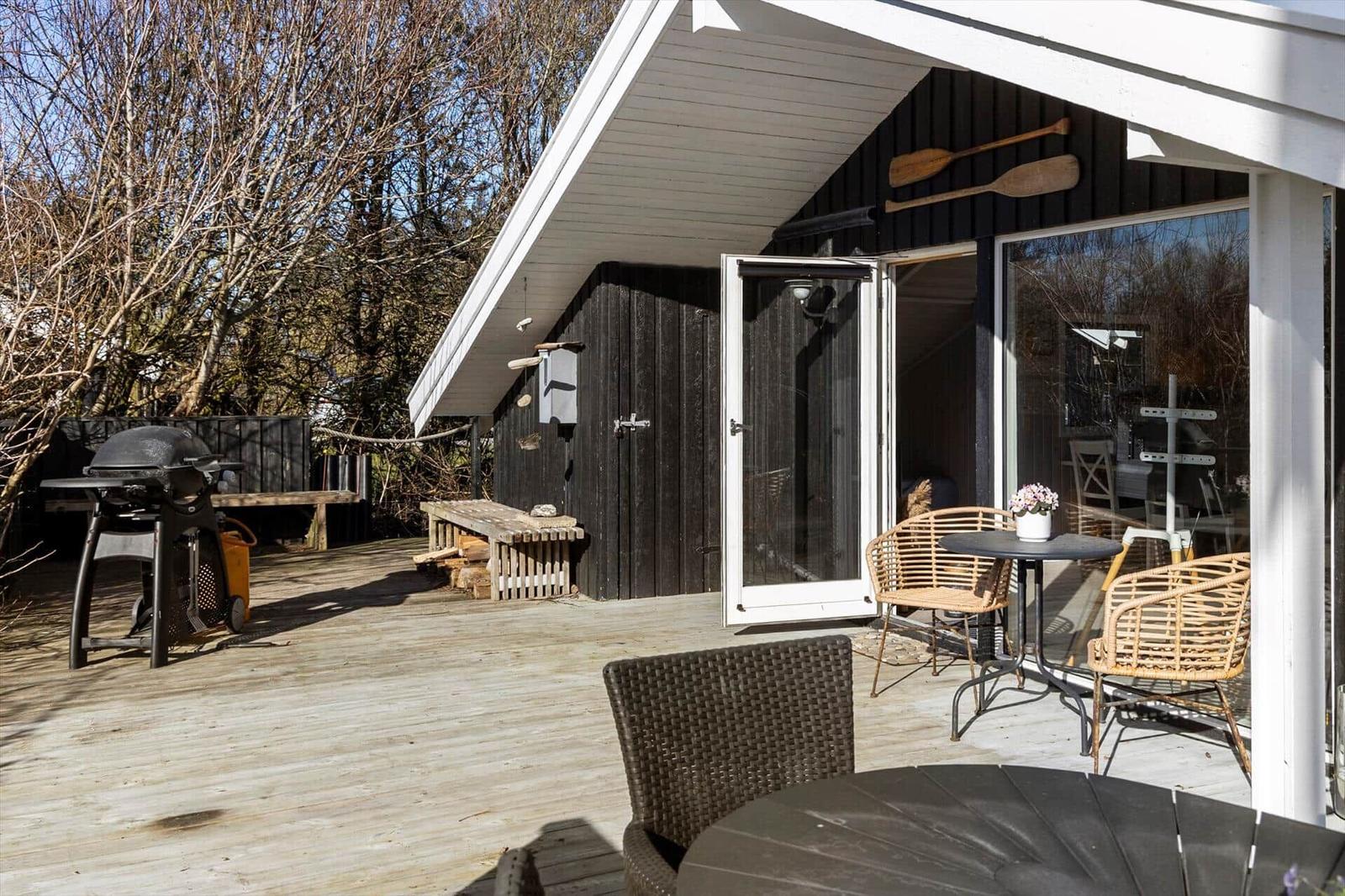 Deck with table, chairs, and grill. Black siding and white roof structure.
