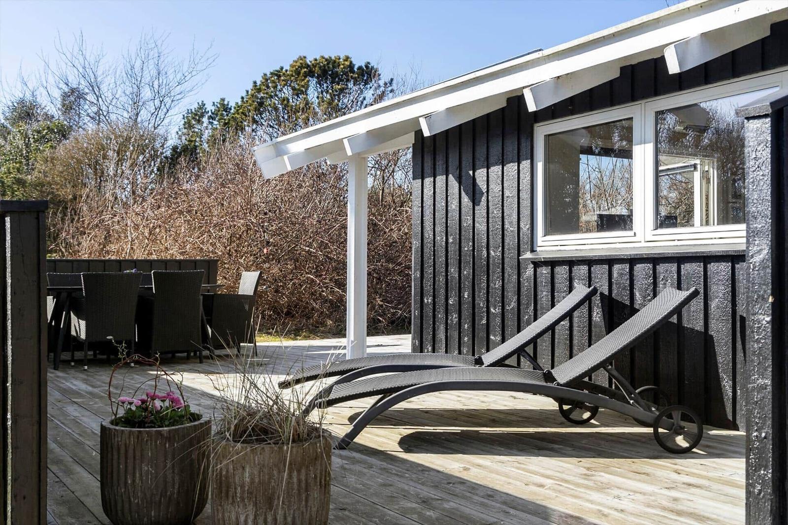 Terrace with lounge chairs, table and chairs. Black wooden wall and plants.