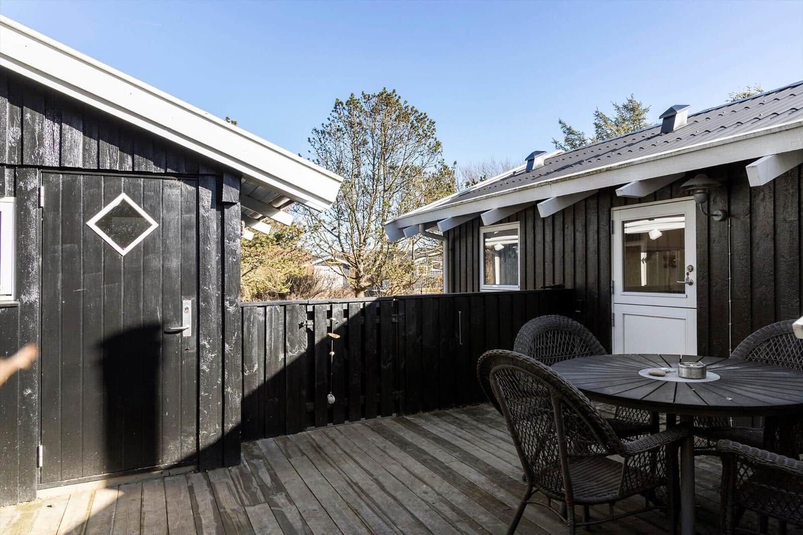 Deck with table and chairs in front of two wooden houses with white doors and roofs.