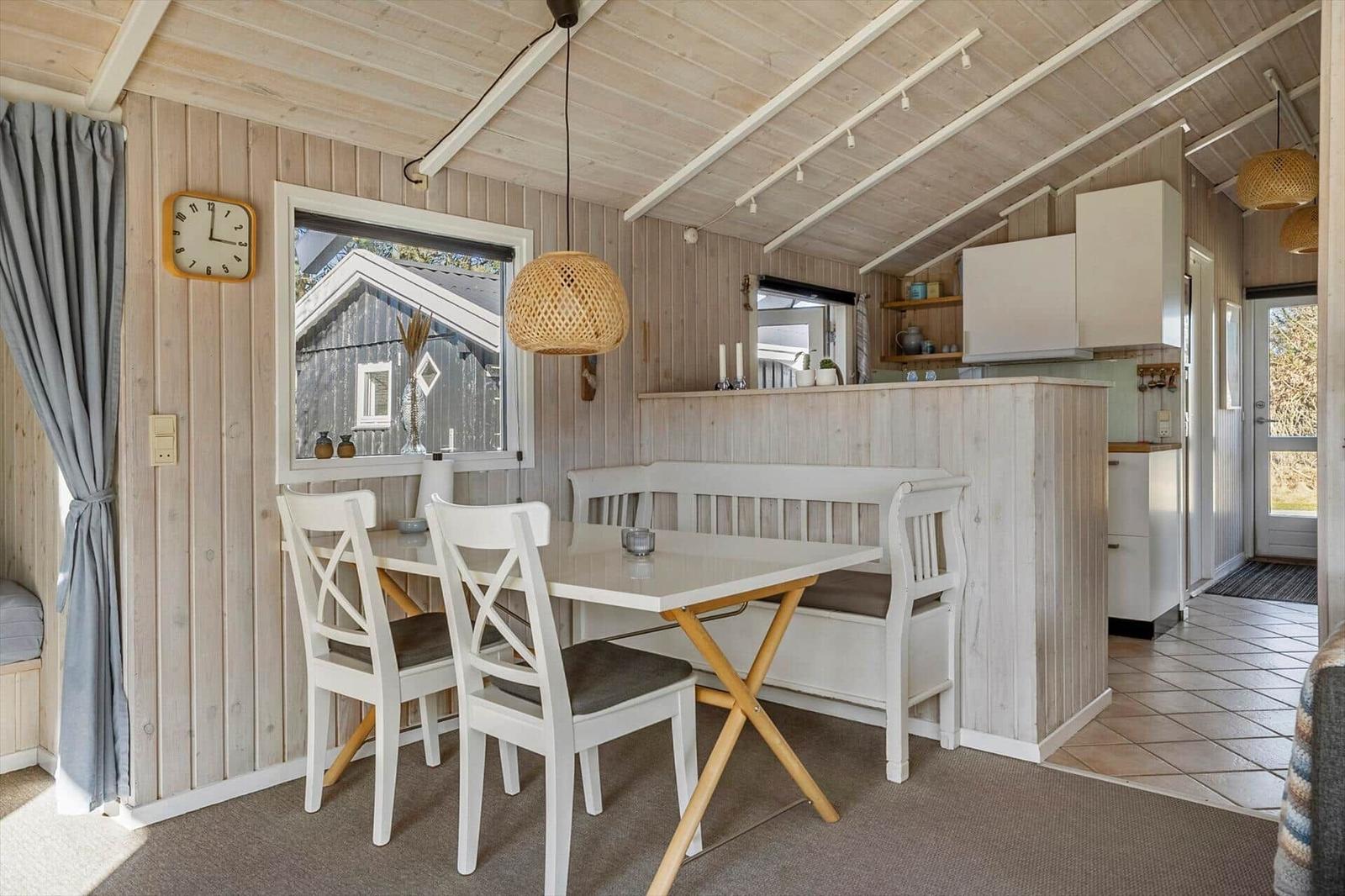 Dining area with table, chairs, and window. Kitchen area in background.