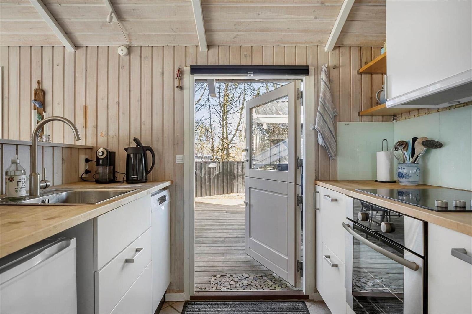 Kitchen with wooden wall, door to balcony, and white cabinets.