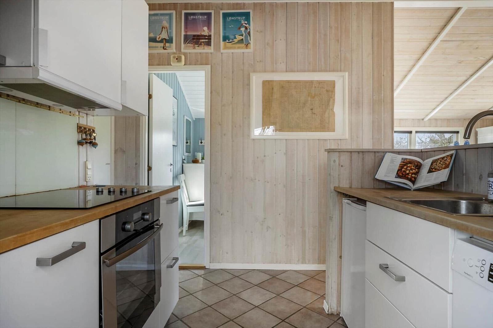 Kitchen with wooden walls, white cabinets, and wooden countertops. Passageway to another room.