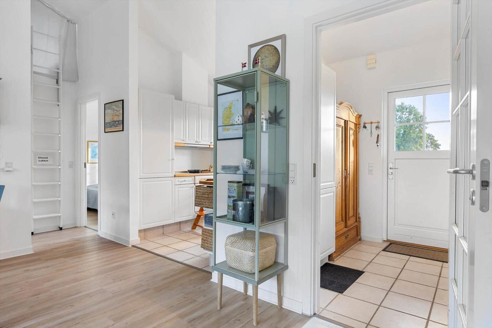 Entrance area with wooden floor, kitchen area, and glass display case with decorative items.
