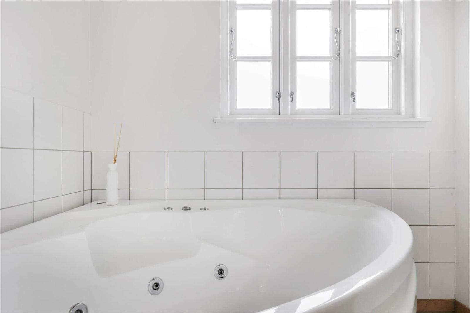 A white bathtub with whirlpool under a window with white frames.
