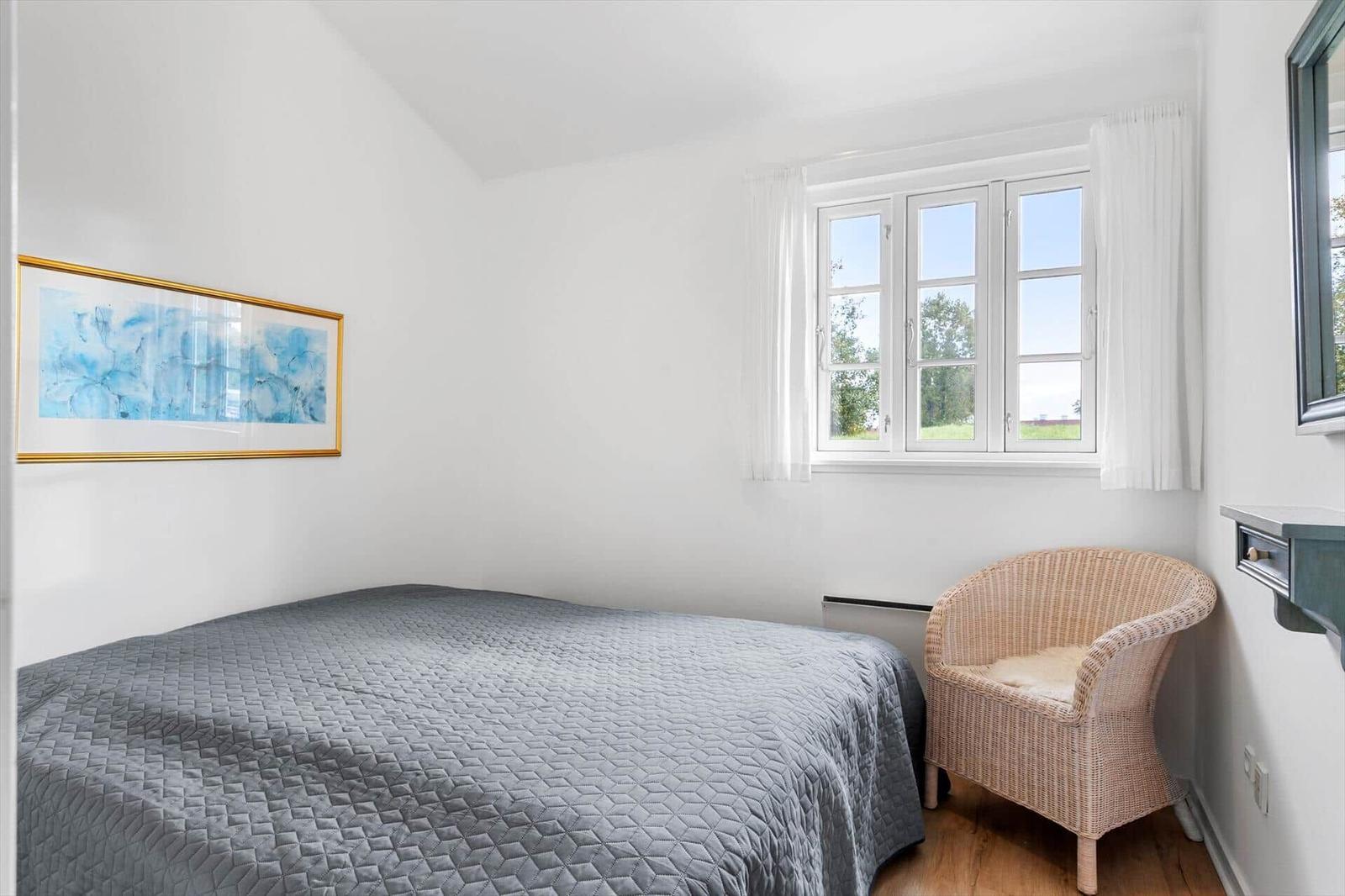 Bedroom with bed, chair, and window. Wall art and wooden floor.