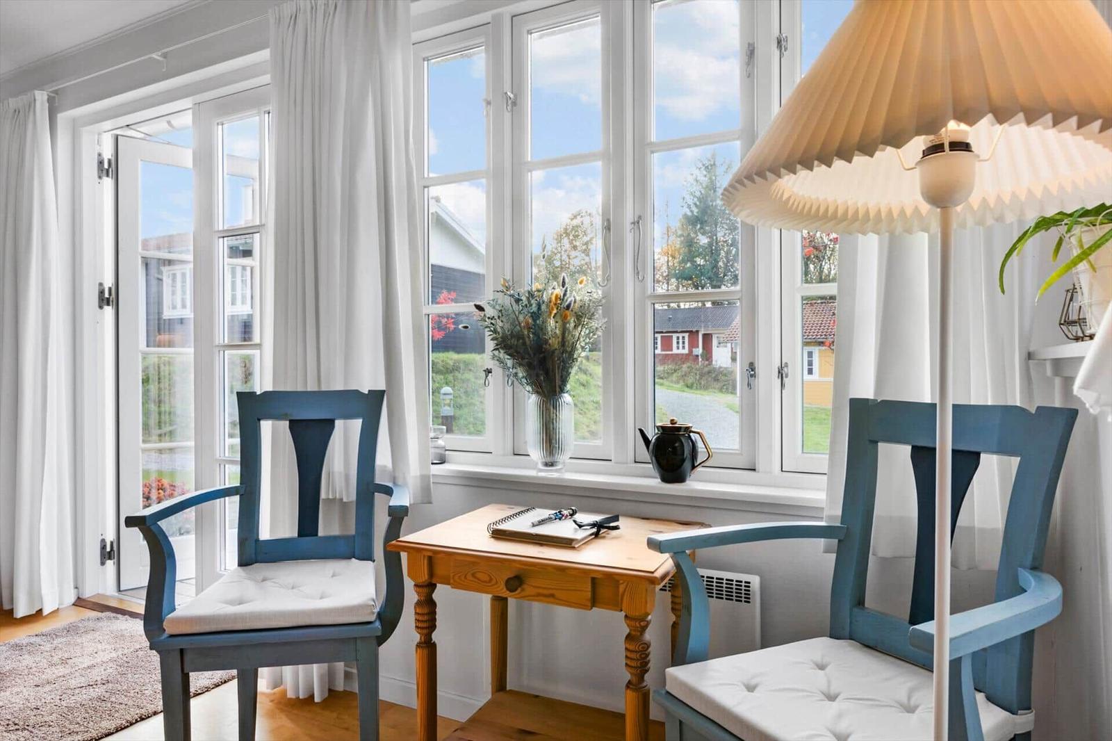 Two blue chairs and a wooden table are by a window overlooking the street.