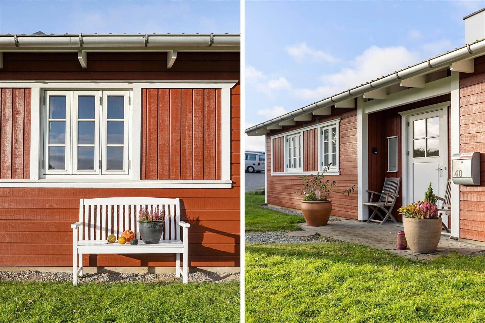 Red wooden house with white window and bench. Entrance with seating and plants.
