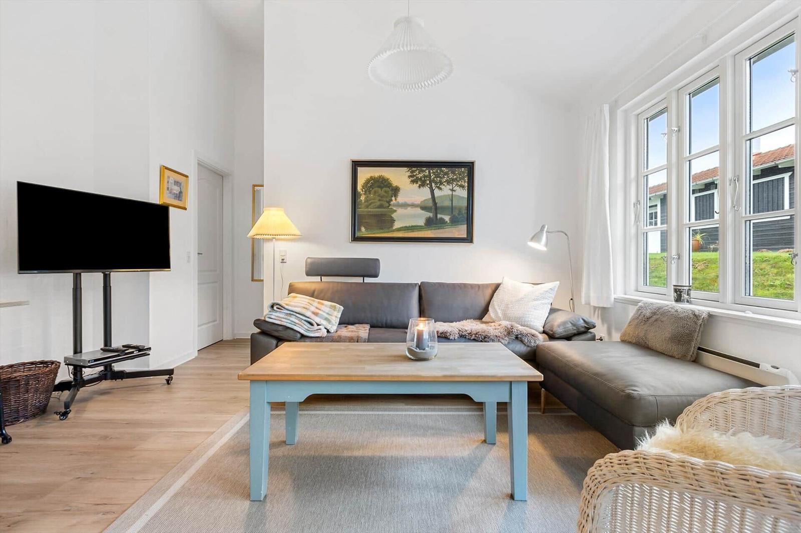 Living room with sofa, coffee table, and TV. Large windows with view of garden.