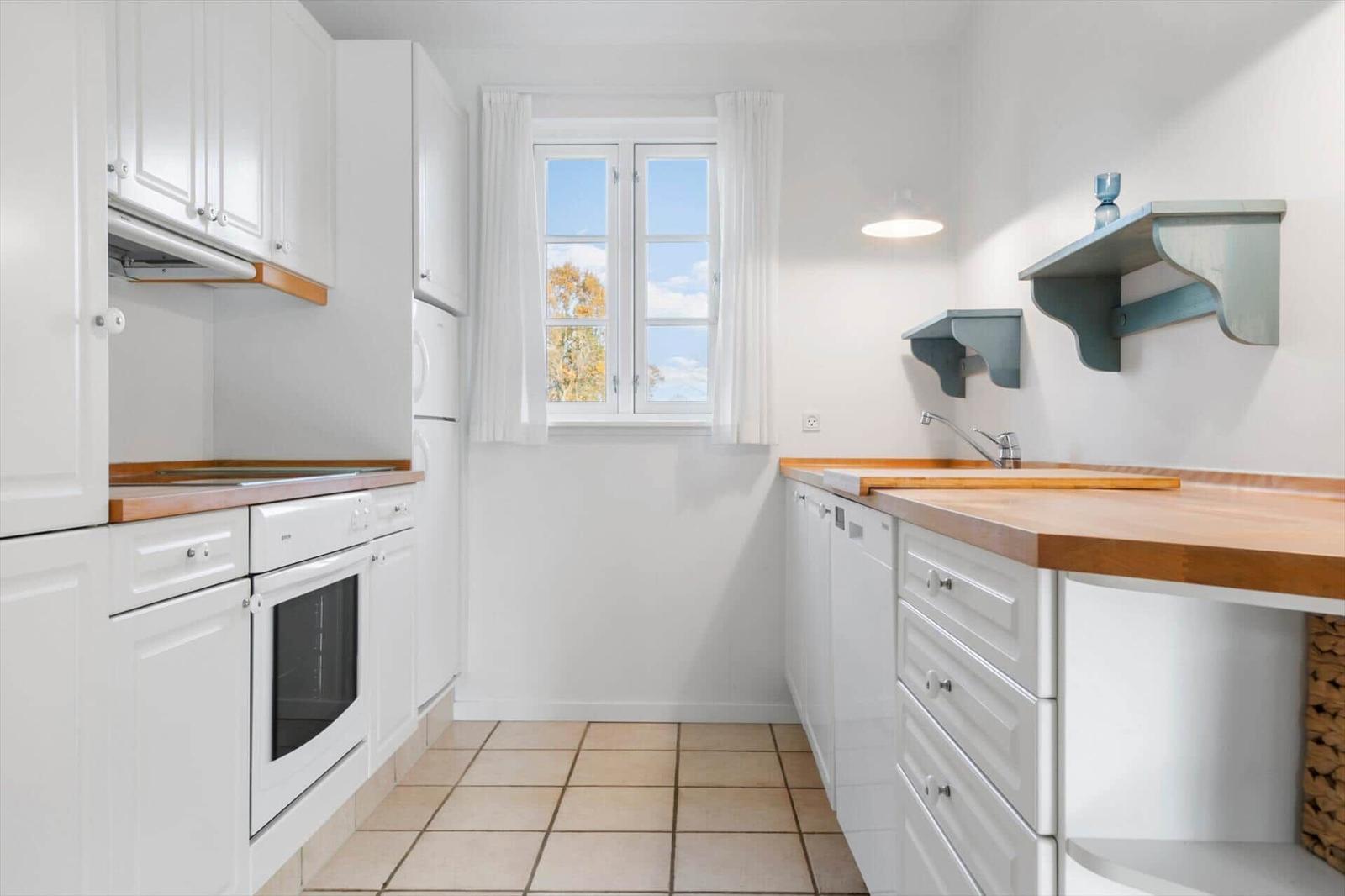 Kitchen with white cabinets, wooden surfaces, and window with view of trees.