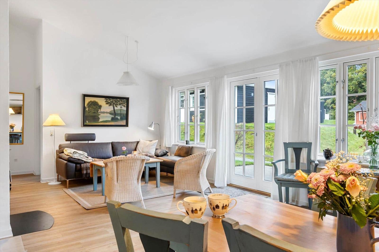 Living and dining area with sofa, tables, and windows to the garden.