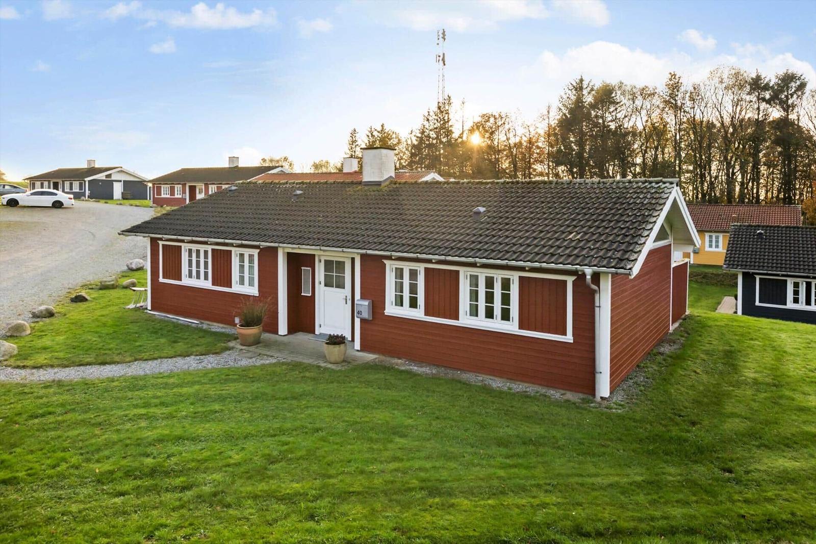 Red wooden house with white window frames and roof, surrounded by grass and trees.