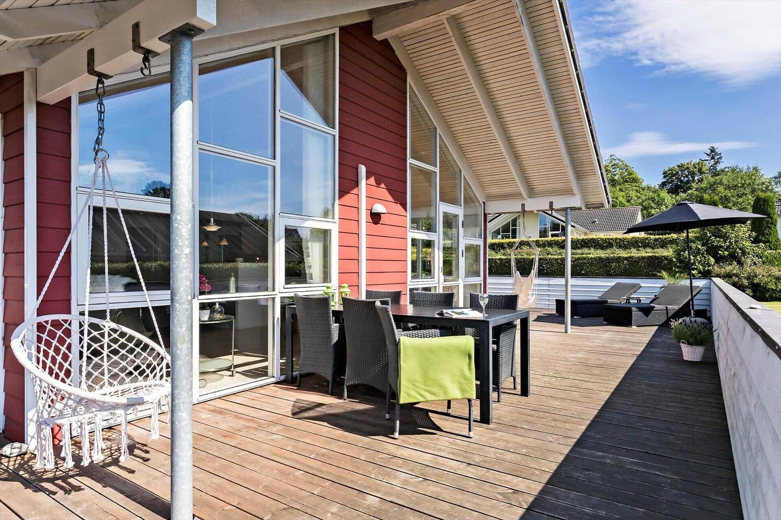 Deck with seating, swing, and sunshade. Wood deck and red siding visible.