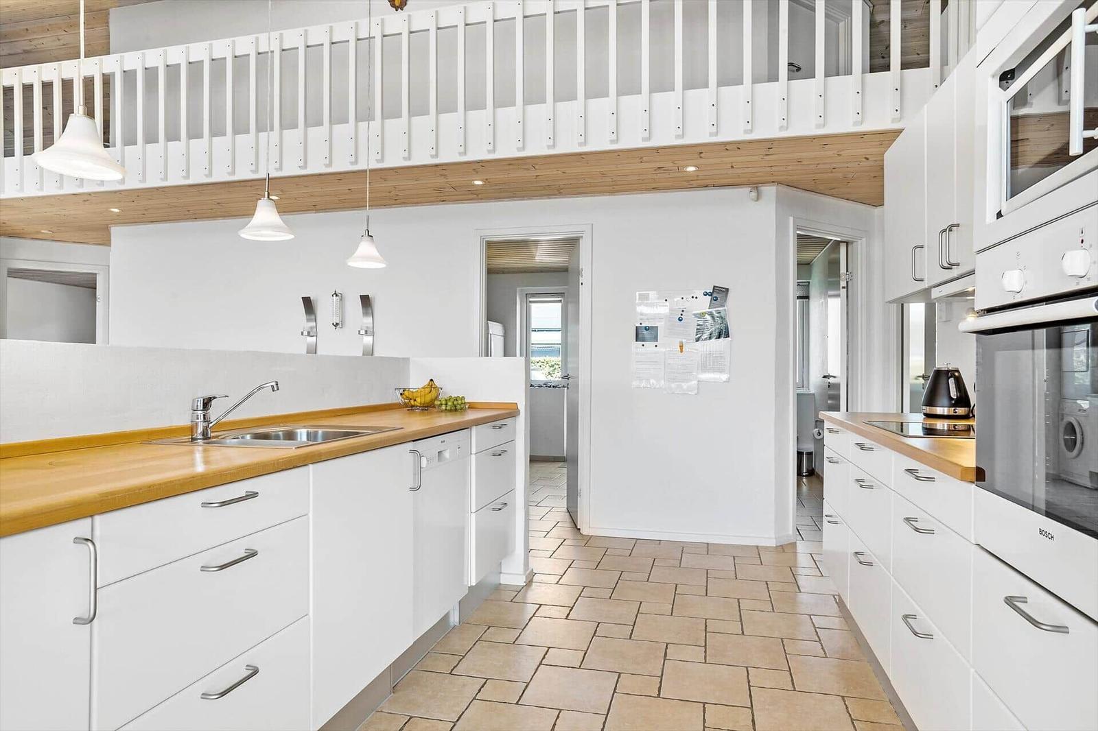 Modern kitchen with wooden countertop and white cabinets. Upper level with wooden railing.