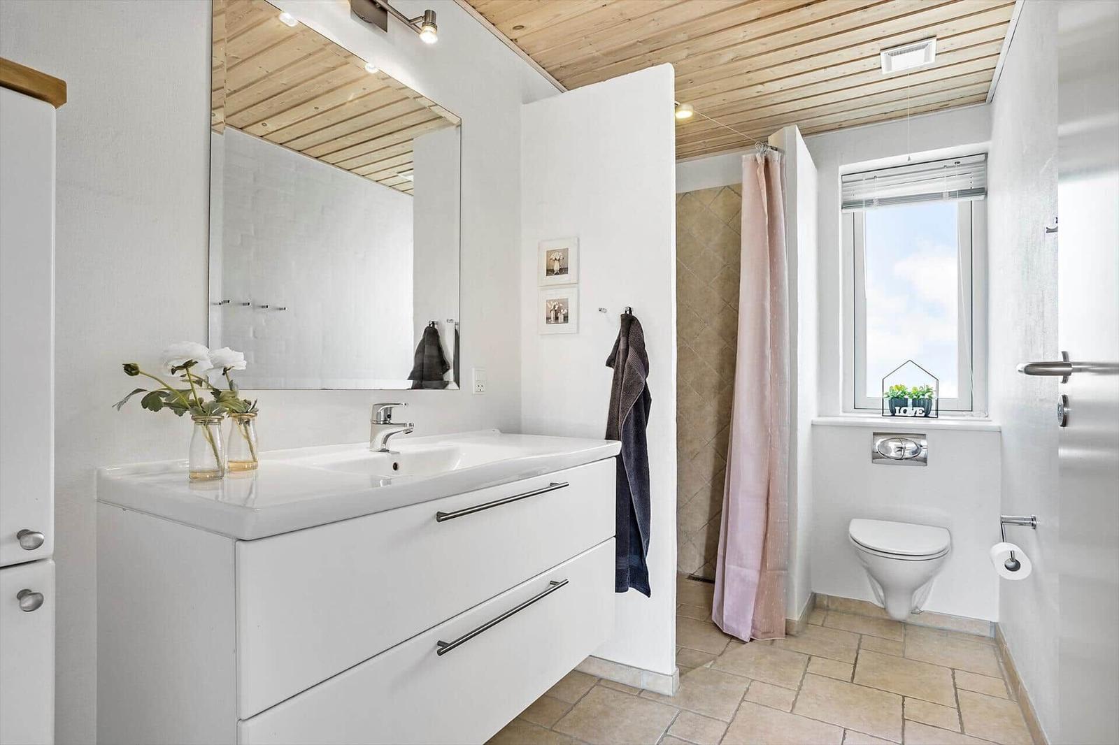Bathroom with sink, shower, and toilet. Wooden ceiling and window with view.