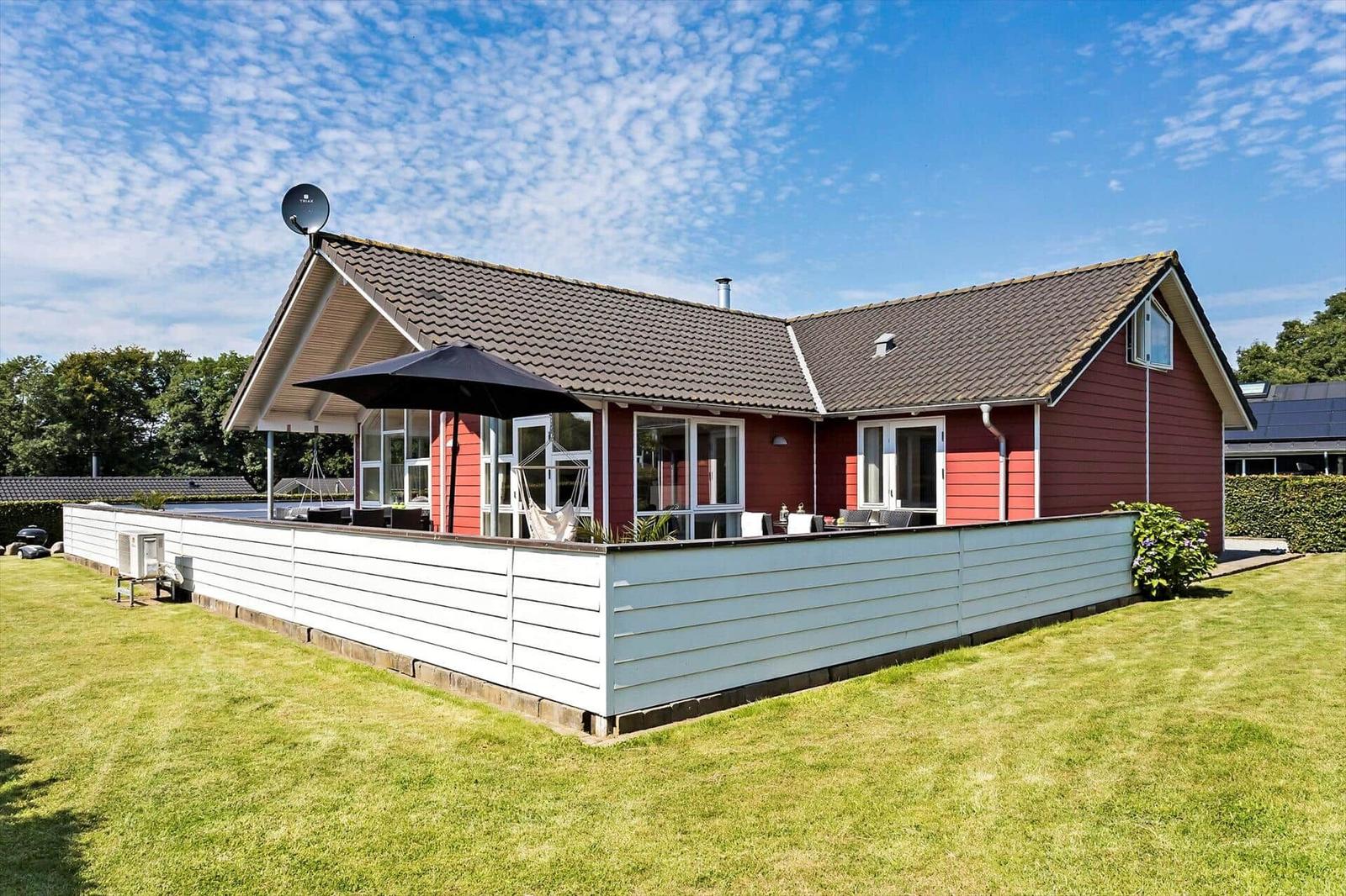 Red house with terrace, garden, and satellite dish under blue sky.