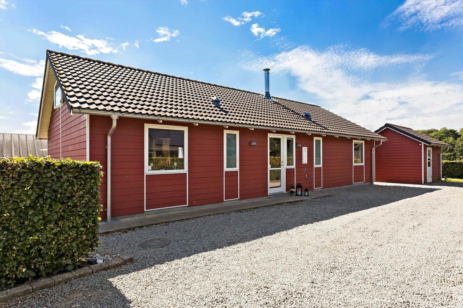 Red house with tiled roof and white door. Gravel yard and hedge.