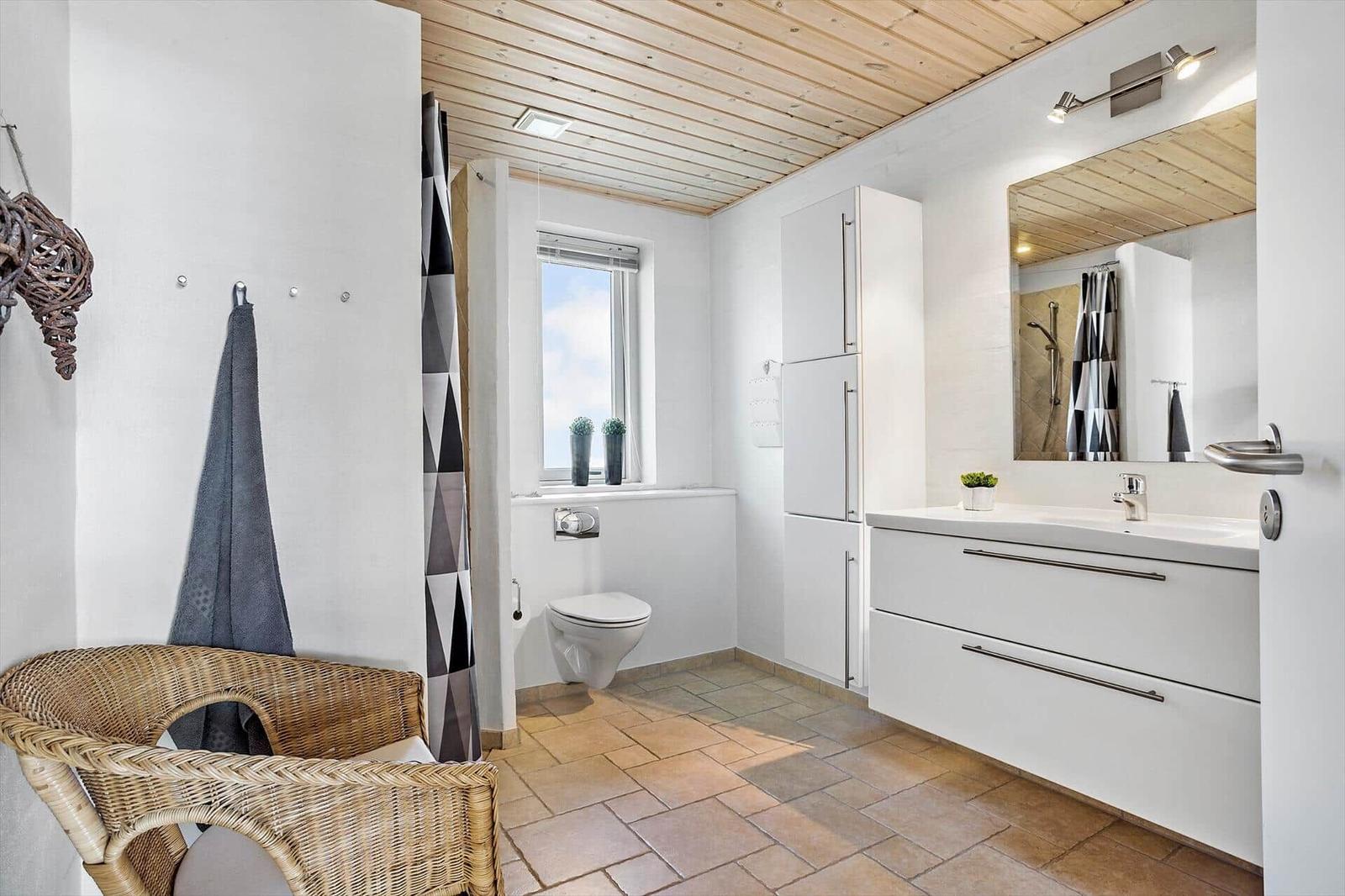 Bathroom with shower, toilet, sink, and wicker chair.
